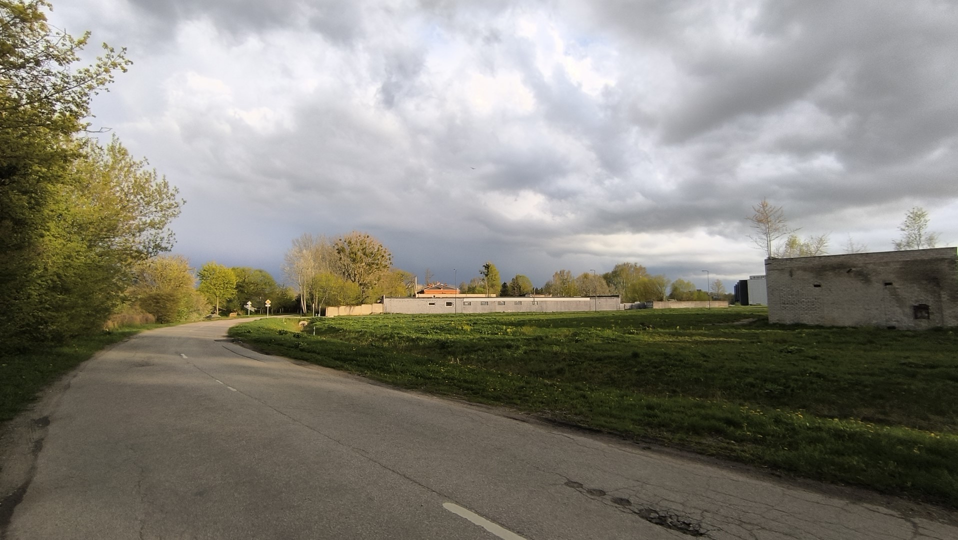 A photo of a landscape. Along the left side of the photo there is a road curving to the right and a building can be seen on the very right.